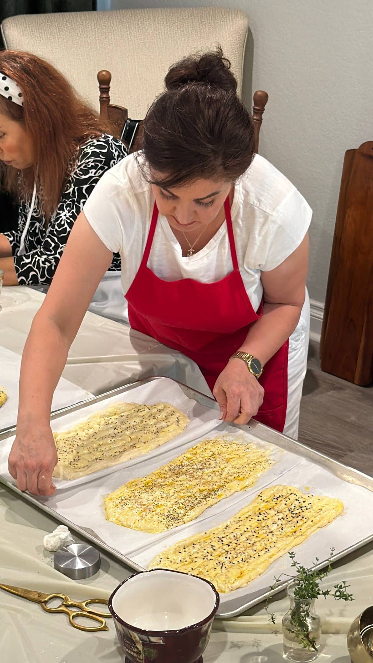 A guest in a red apron seeding three trays of shaped barbari dough