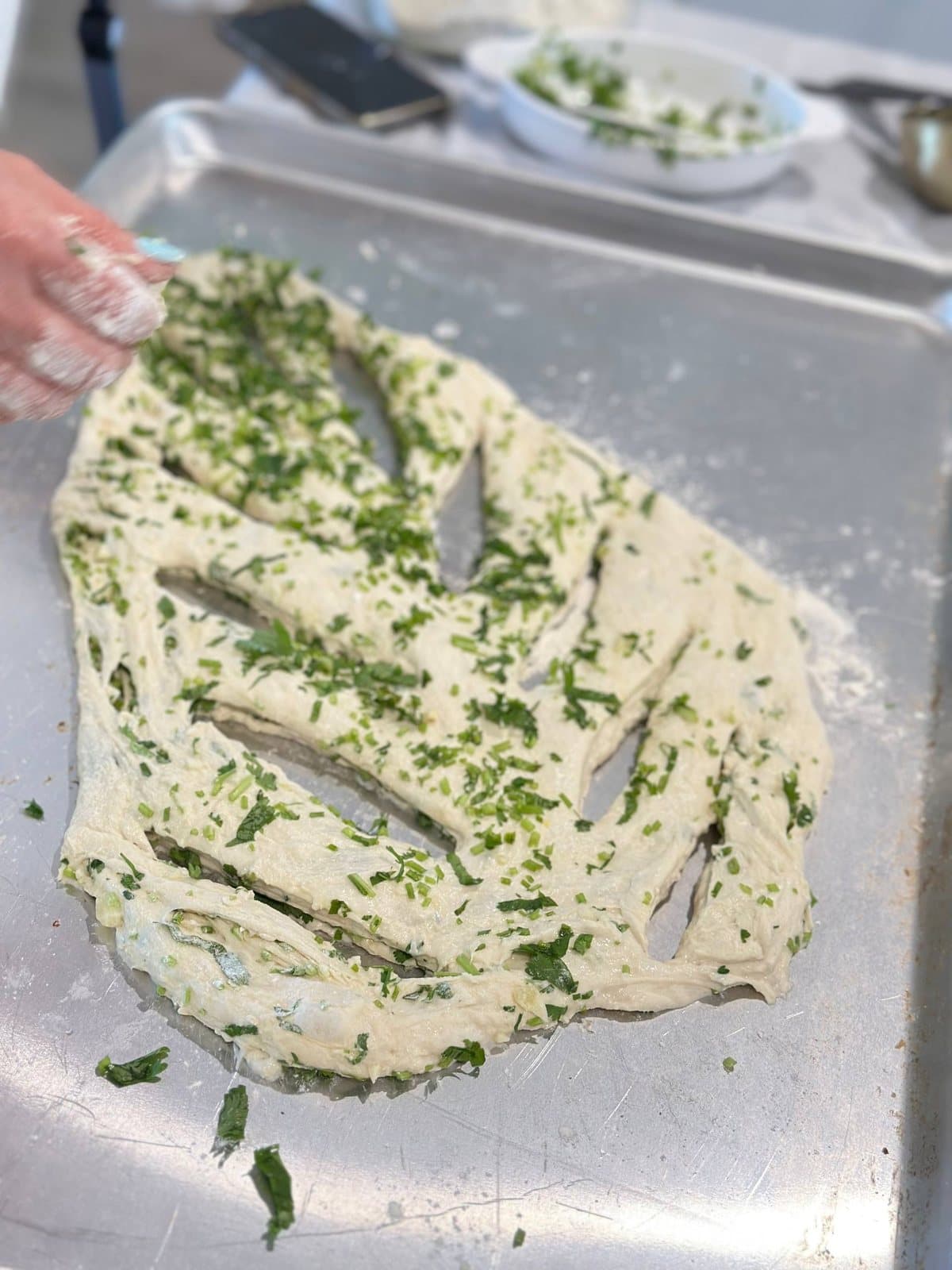 Scattering chopped herbs over slashed barbari dough before it goes in the oven