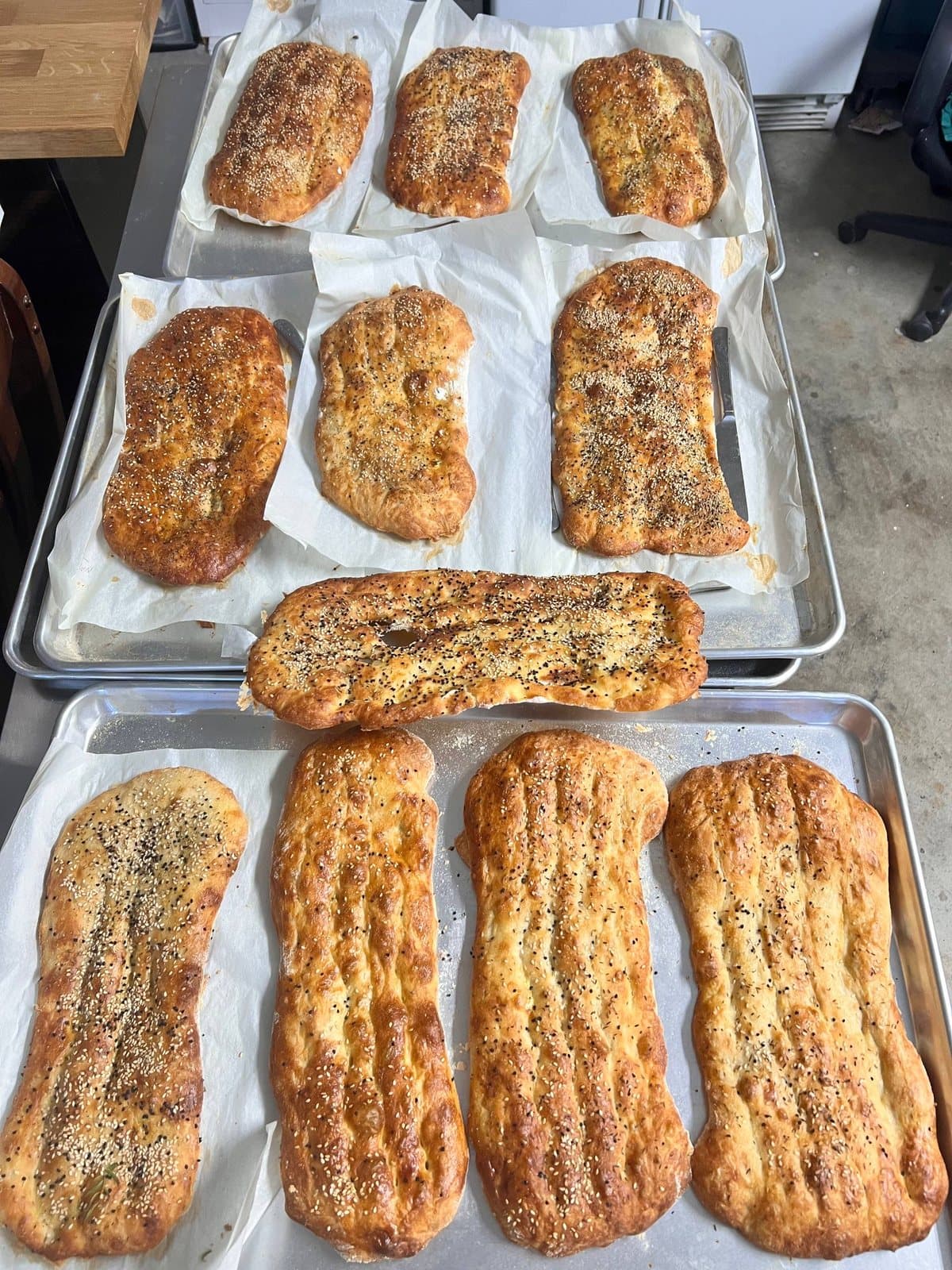 Three trays of finished barbari, dimpled and dusted with sesame and nigella