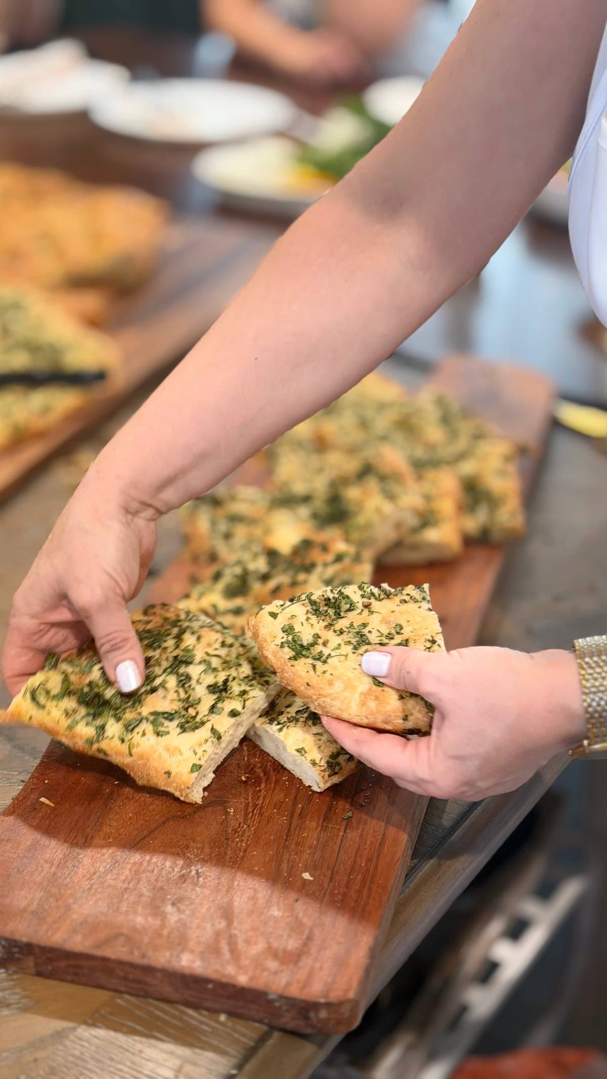 Hands breaking warm herb bread apart on a wooden board